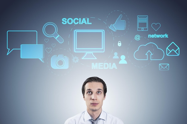 Portrait of thoughtful young businessman with creative social media hologram on blue background Communication and network concept