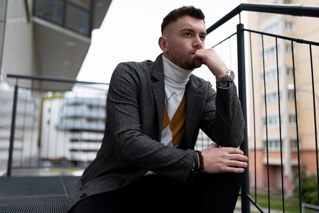 Portrait of a thoughtful young man sitting on the steps next to his own building