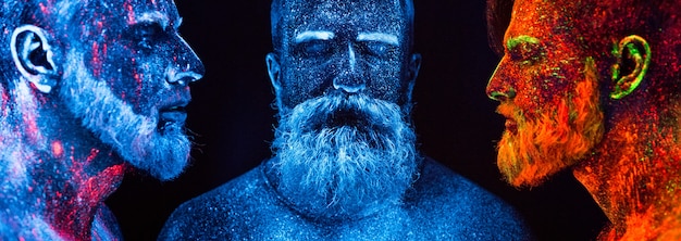Photo portrait of three bearded men painted in florescent powders.