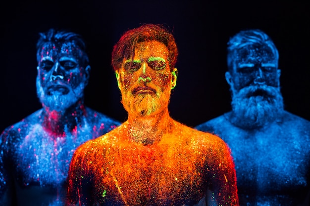 Portrait of three bearded men painted in florescent powders.