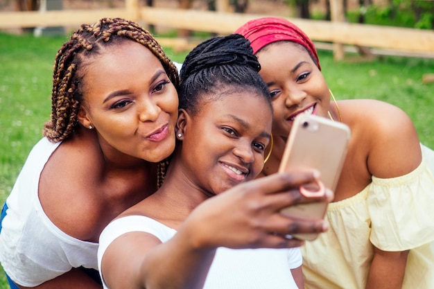 Portrait of three beautiful african-american women afro braids dreadlocks and turban taking pictures of yourself on the phone in the park at a picnic,sisters on vacation