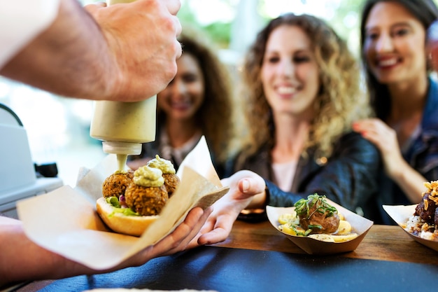 Portrait of three beautiful young women buying meatballs on a food truck in the park.