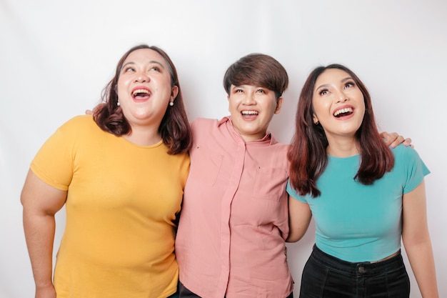 A portrait of three friends looks excited pointing at the copy space upside them isolated by white background