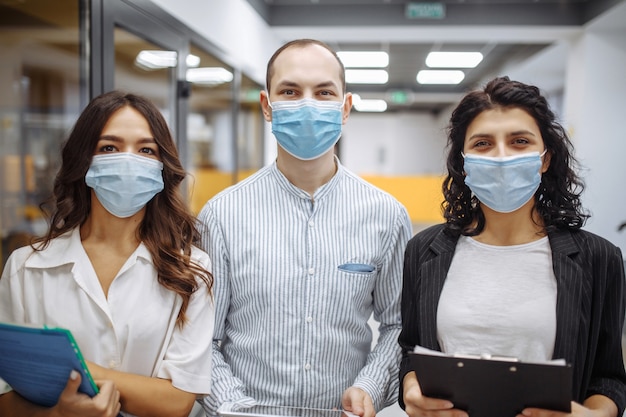 Портрет трех офисных работников в медицинских масках, обсуждающих бизнес и перспективы на будущее.