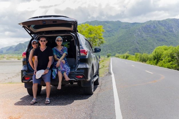 Portrait of three people sitting on back of a truck in countryside road trip