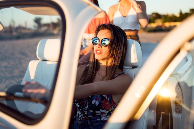 Portrait of three pretty young women driving on road trip on beautiful summer day.