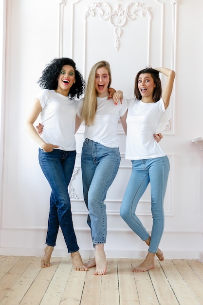 Portrait of three seductive multiethnic women standing together and smiling at camera isolated over white background