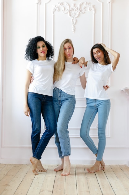 Portrait of three seductive multiethnic women standing together and smiling at camera isolated over white background