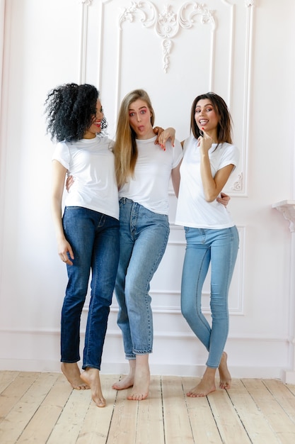 Portrait of three seductive multiethnic women standing together and smiling at camera isolated over white background