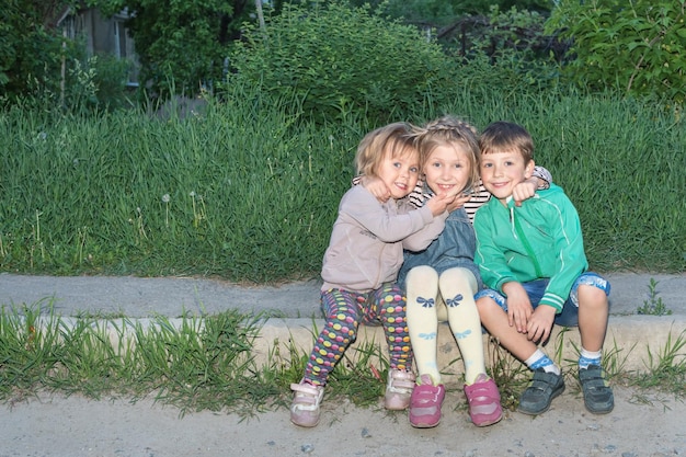 縁石に座って抱きしめる3人の小さな楽しい子供たちの肖像画