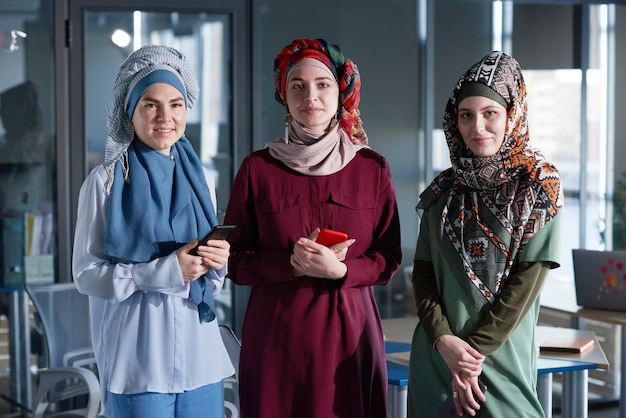 Portrait of three women in hijabs looking at camera while standing together at office