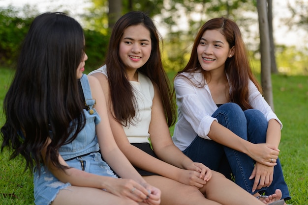 Portrait of three young Asian women as friends together relaxing at the park outdoors