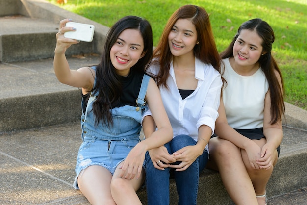 Photo portrait of three young asian women as friends together relaxing at the park outdoors