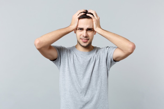 Portrait of tired displeased young man in casual clothes, putting hands on head 