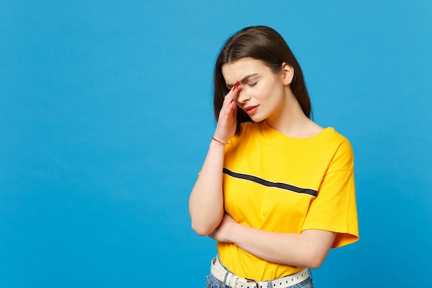 Portrait of tired exhausted young woman in vivid casual clothes keeping eyes closed, putting hand on nose isolated on bright blue background in studio. People lifestyle concept. Mock up copy space.