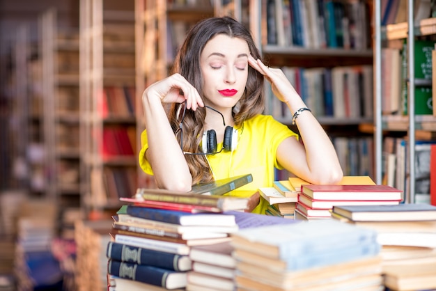 Портрет усталой студентки, занимающейся с книгами в библиотеке