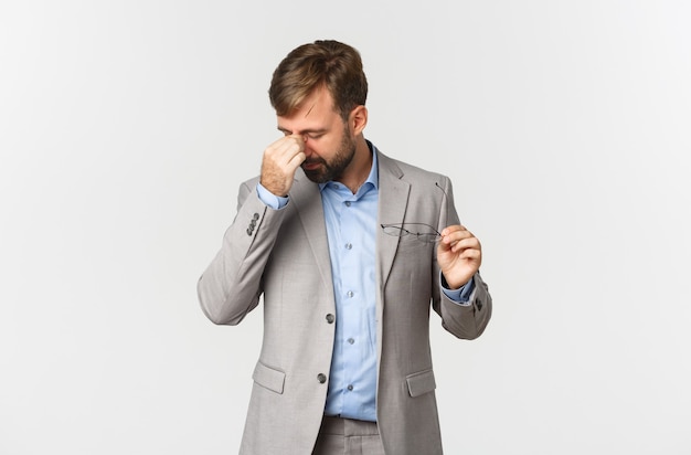 Portrait of tired male entrepreneur in grey suit, taking-off glasses and rubbing eyes