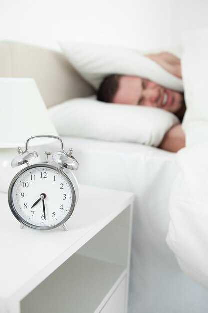 Photo portrait of a tired man covering his ears with a pillow