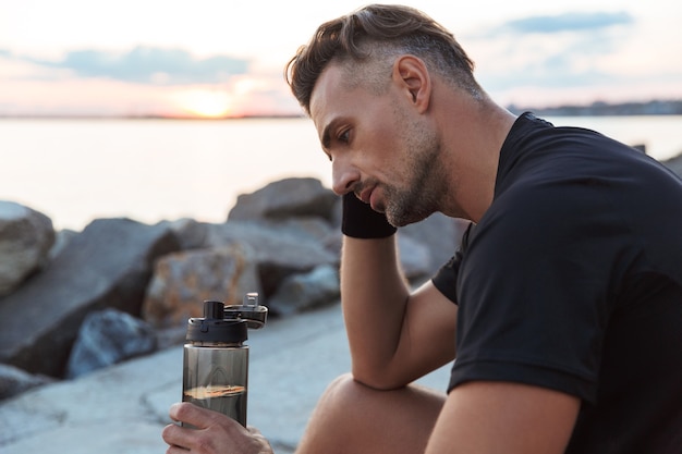 Portrait of a tired sportsman drinking water