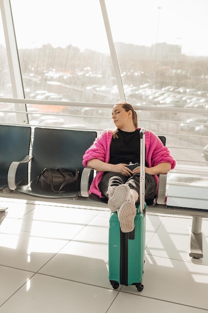 Photo portrait of tired woman wearing pink cardigan sitting on chair stretching legs on turquoise suitcase