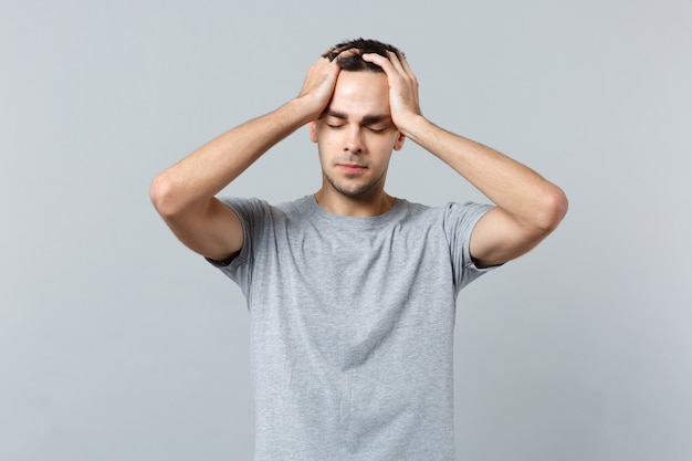 Portrait of tired young man in casual clothes keeping eyes closed, putting hands on head 