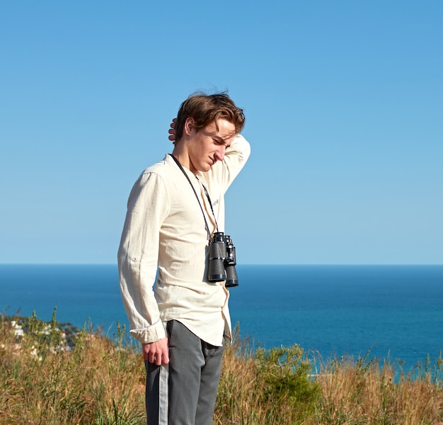 A portrait of a tired young man with binoculars hanging around his neck