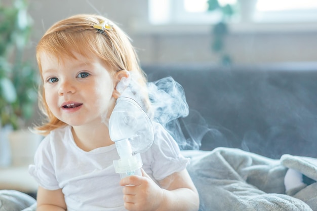 La ragazza del bambino del ritratto tiene in mano una maschera da un nebulizzatore e sorride seduta a casa