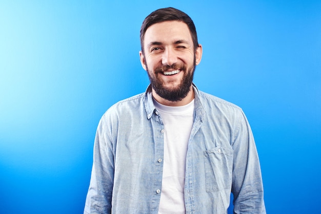 Portrait of toothy smiling and joyfully laughing handsome caucasian brutal bearded man dressed in casual isolated on blue background
