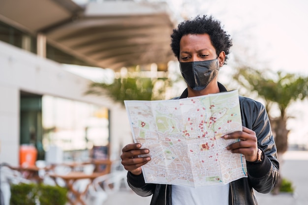 Ritratto di uomo turistico che indossa una maschera protettiva e cerca indicazioni sulla mappa mentre si cammina all'aperto per strada