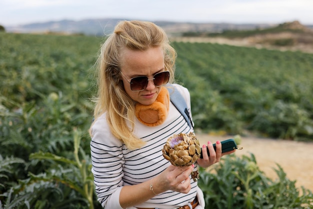 観光客の女性のポートレートは、電話でアーティチョークの写真を撮ります