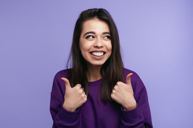 Portrait of trendy young woman showing thumb up over violet