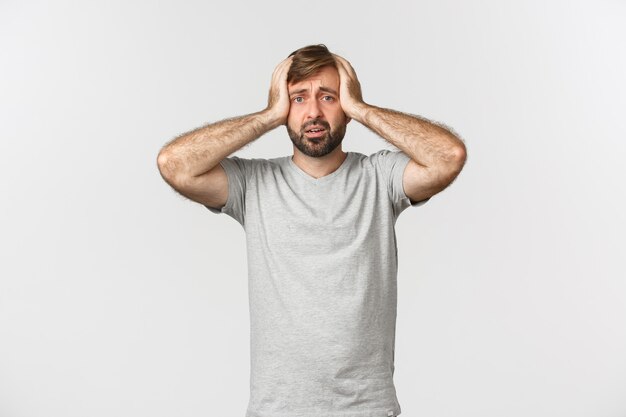 Portrait of troubled man having panic, holding hands on head and standing alarmed over white.