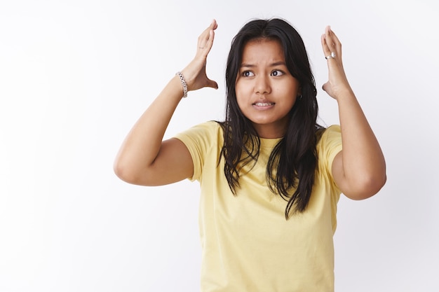 Portrait of troubled and stressed young female student under pressure during exams and work shaking hands around head and clenching teeth distressed, perplexed looking nervously left over white wall