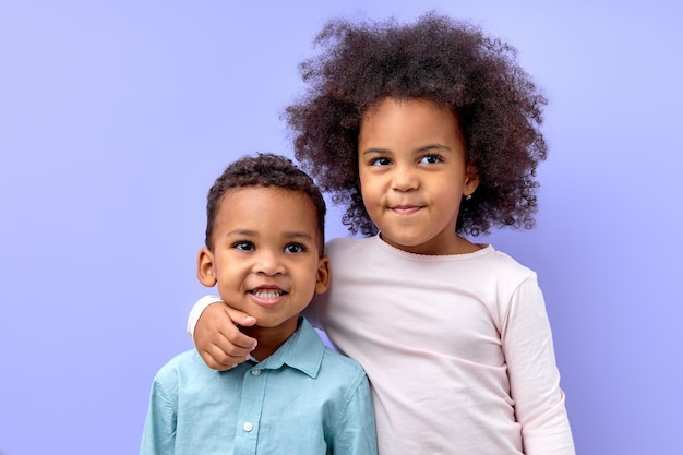 Portrait of two adorable siblings brother and sister hugging each other isolated on purple studio ba