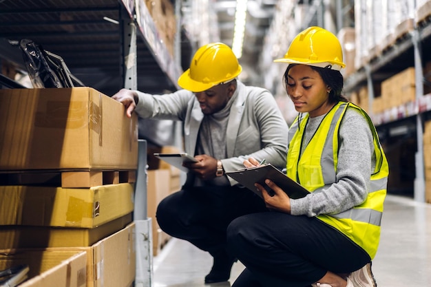 Portrait two african american engineer team shipping order\
detail on tablet check goods and supplies on shelves with goods\
inventory in factory warehouselogistic industry and business\
export