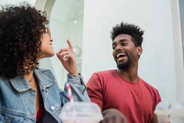 Portrait of two Afro friends having fun together and enjoying good time while drinking fresh fruit juice outdoors at cafeteria.