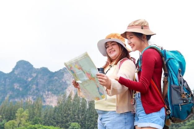 Foto ritratto di due donne asiatiche che trasportano zaini in piedi guardando la mappa per viaggiare nella natura