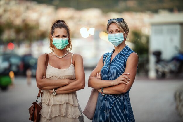 Portrait of a two attractive female friends who wear a surgical mask while exploring the wonderful city of Meditteranian.