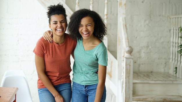 Portrait of two beautiful african american girls laughing and looking into camera at home