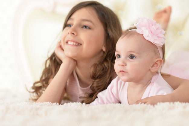 Photo portrait of two beautiful cute sisters posing in bed at home