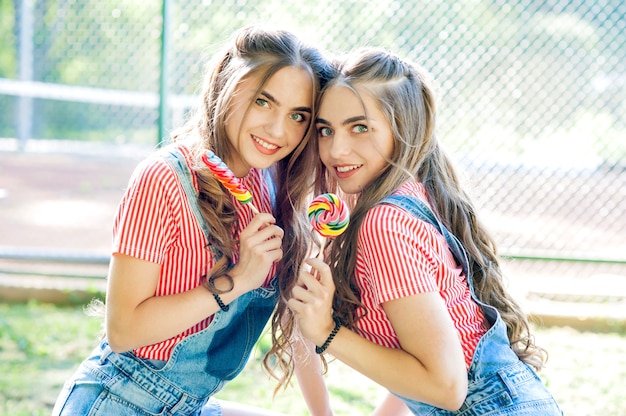 Photo portrait of two beautiful girls twins with lollipop caramel