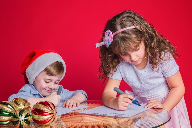 Ritratto di due bellissimi bambini felici che scrivono una lettera a babbo natale.