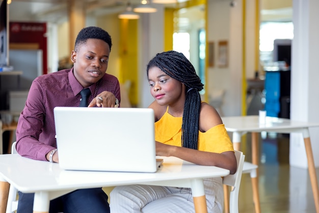 Portrait of two black students with netbook sitting at home interior, african american using laptop computer for searching information and making booking