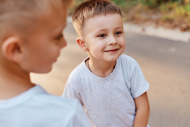 Portrait of two boys, siblings, brothers and best friends wearing white casual style t-shirts posing outdoors, spending free time together, children expressing happiness.