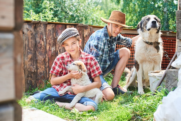 Portrait of two brothers sitting in the place with dogs on the grass in the village