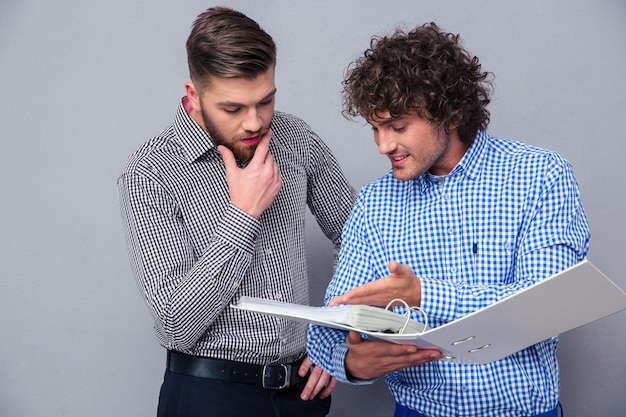 Portrait of a two casual businessmen reading documents in folder over gray wall