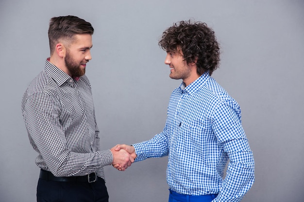 Photo portrait of a two casual men doing handshake over gray wall
