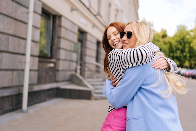 Portrait of two cheerful emotional woman friends hugging and feeling happy in city street after long separation Best girlfriends feeling joyful and happy together Concept of woman friendship
