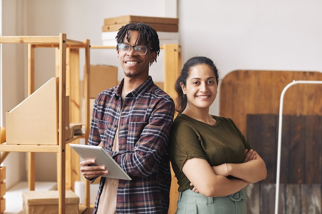 Portrait of two colleagues standing with arms crossed back to back and smiling at camera they working in delivery service