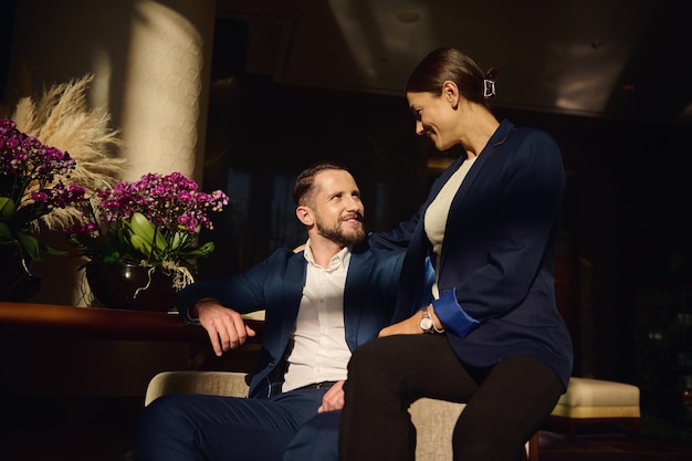 Portrait of two confident people, couple on honeymoon,colleagues on business trip, Caucasian woman and man, business partners talking together sitting on armchair in the lounge zone of a luxury hotel